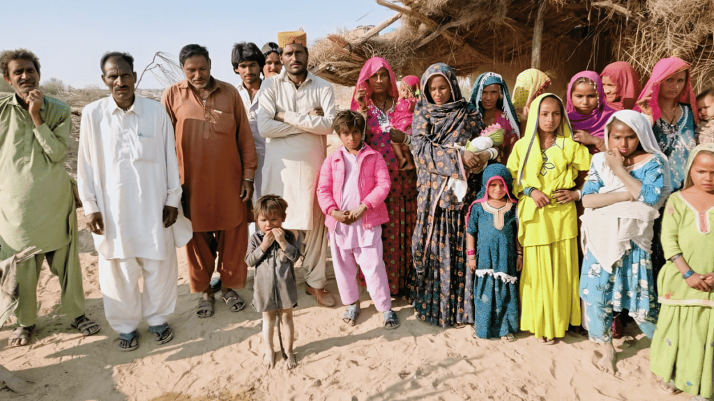A diverse group of new Marwari converts, men, women, and children, standing solemnly in their village, showcasing a mix of traditional clothing and new faith.