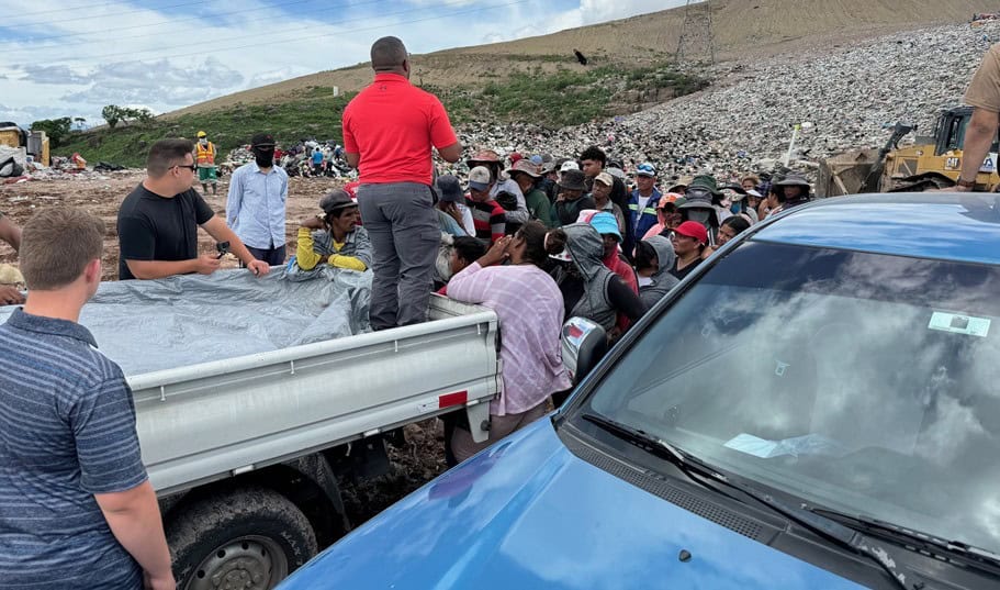 A missionary group distributes food and supplies to a large crowd of people gathered around a truck at a garbage dump in Honduras.