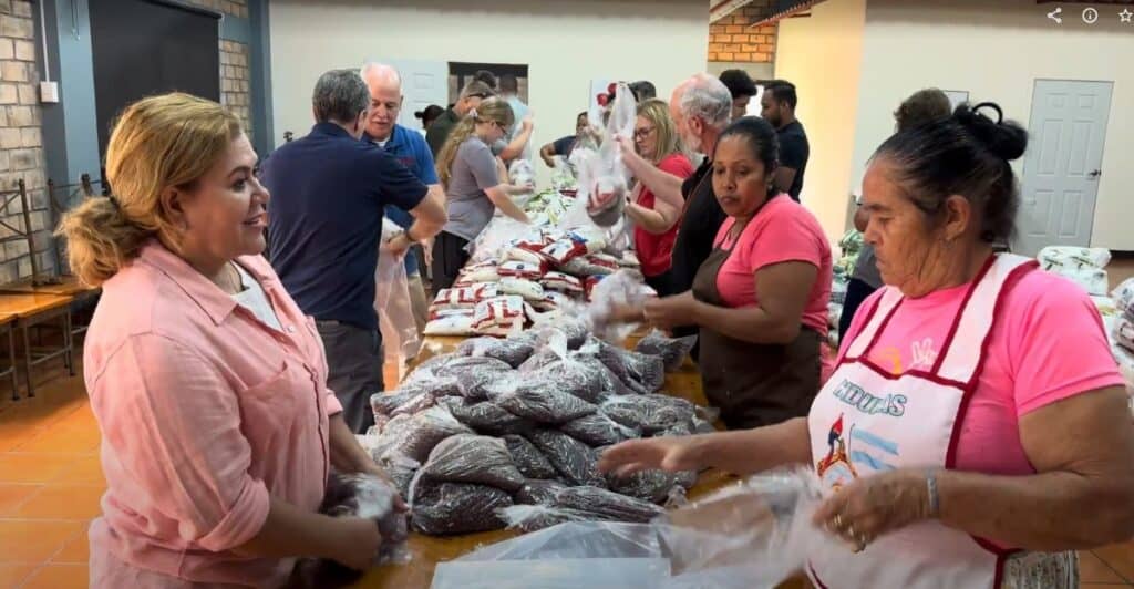 Volunteers work together in a room, assembling food bags filled with rice and beans for distribution in Honduras.