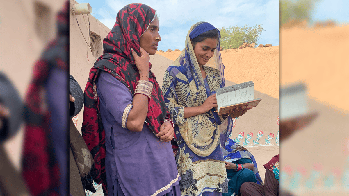 Two Marwari women, a mother in purple and her teenage daughter, share a moment of worship outside their home, as the daughter leads in song.