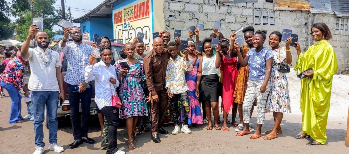 A group of people in the Democratic Republic of Congo holding up their new Bibles outside a church, smiling and celebrating.