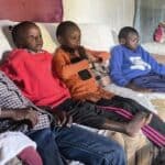 Four children sitting on a couch inside a modest home, watching something attentively.