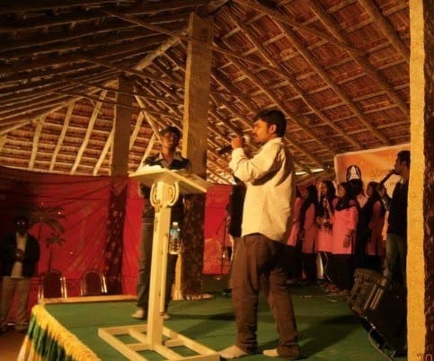 Here Raghu is seen preaching at one of the village churches he started that has outgrown the house they first met in. Now they have a bamboo building with wooden rafters and a grass ceiling. The floor is packed dirt.