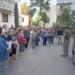 A group of people have gathered outside and are listing to a person preach a message. They are to receive food and a Bible.