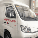 A white Forland medical mission vehicle designed for outreach services, parked indoors. The vehicle features an 18-foot body with "Forland" branding on the side, equipped to carry medical supplies and a dedicated team to remote areas.