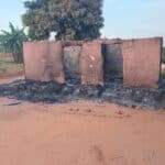 The remains of a burned down house. All that remains are the side walls. Blackended dirt surrounds the outside and inside of the building which no longer has a roof.