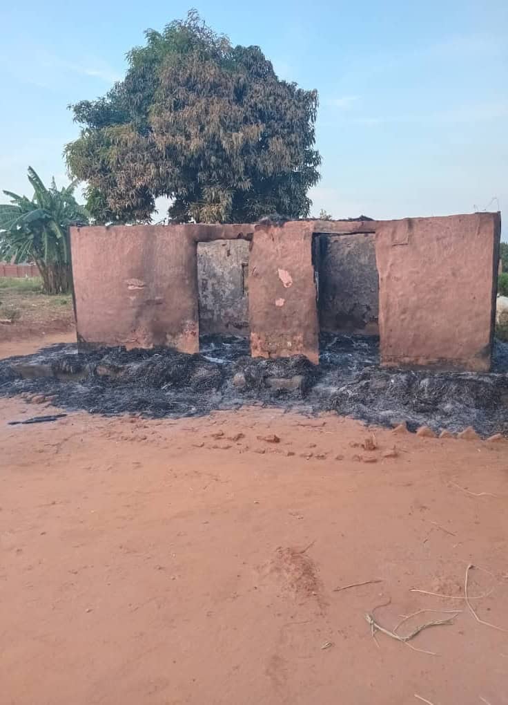 The remains of a burned down house. All that remains are the side walls. Blackended dirt surrounds the outside and inside of the building which no longer has a roof.